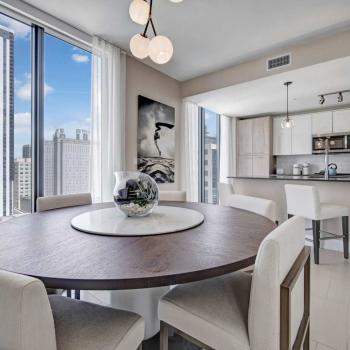 Elegant dining area with modern furnishings, large windows offering city views, and a round wooden table in Parkline Miami luxury apartments.