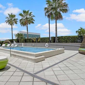 A rooftop pool with palm trees and lounge chairs at Parkline Miami Luxury Apartments, featuring a modern tiled pool deck and clear blue skies.