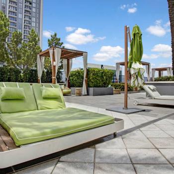 A spacious lounge area at Parkline Miami Luxury Apartments with green cushioned daybeds and wooden cabanas, surrounded by lush greenery.