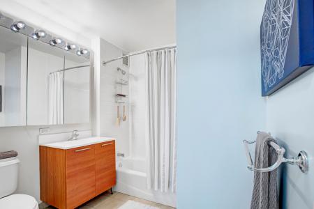 A pristine bathroom with a modern vanity, full-size mirror, and a tiled shower with a curtain, blending functionality with contemporary design.