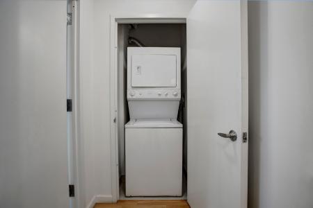 A compact laundry area featuring a stacked washer and dryer unit tucked behind white closet doors, offering convenient in-home laundry access at Skyline New Rochelle Luxury Apartments.