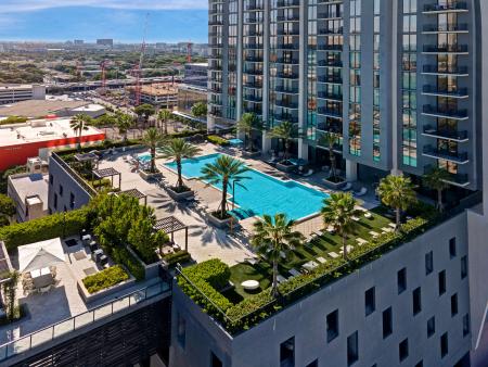 A stunning rooftop pool deck crowns the Parkline Miami tower, featuring a large resort-style pool surrounded by lush palm trees, shaded lounge areas, and cozy seating alcoves. Elevated above the city, this vibrant oasis offers panoramic views of the Miami skyline and creates the perfect retreat for urban relaxation.