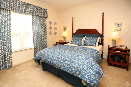 Sunlit bedroom with large window, matching blue curtains and comforter, and traditional wooden bed frame