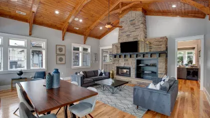  Spacious community lounge featuring high vaulted wooden ceilings, modern furnishings, a cozy stone fireplace, and large windows that fill the space with natural light, creating a warm and inviting atmosphere.