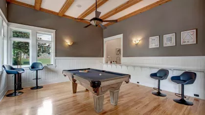 Stylish game room featuring a pool table, modern seating, and large windows, with wood accents and contemporary decor creating a welcoming space for relaxation and socializing.