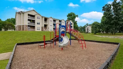 Colorful playground surrounded by lush green grass and modern apartment buildings, offering a fun and safe outdoor space for children to play.