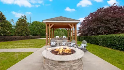Outdoor fire pit area with comfortable seating and a covered pavilion, surrounded by lush greenery, offering a perfect spot for gatherings and relaxation in a serene setting.