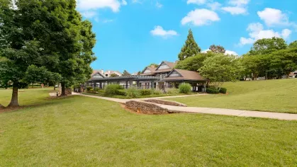 Expansive green lawn with mature trees and a walking path leading to a covered pavilion, creating a peaceful and inviting outdoor space for residents to relax and enjoy nature.