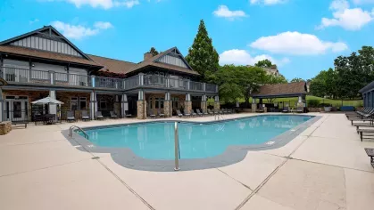  Resort-style swimming pool surrounded by spacious sundeck areas and modern clubhouse, offering a relaxing outdoor space with lush greenery and a bright blue sky.