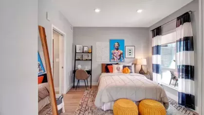  Spacious bedroom with gray bedding, bold artwork, and yellow poufs.