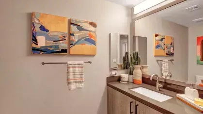  A bathroom featuring a sleek sink, colorful abstract art, and potted plants.