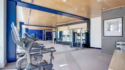 Modern gym with stationary bikes, treadmills, and strength machines in a brightly lit room with mirrors and blue accents.