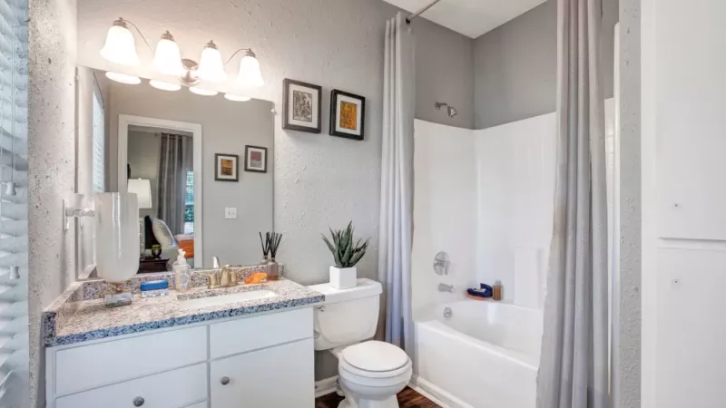 A modern bathroom featuring a sleek granite countertop, a well-lit vanity with elegant lighting, a white bathtub with a shower curtain, and warm wood-style flooring for a clean and inviting look.
