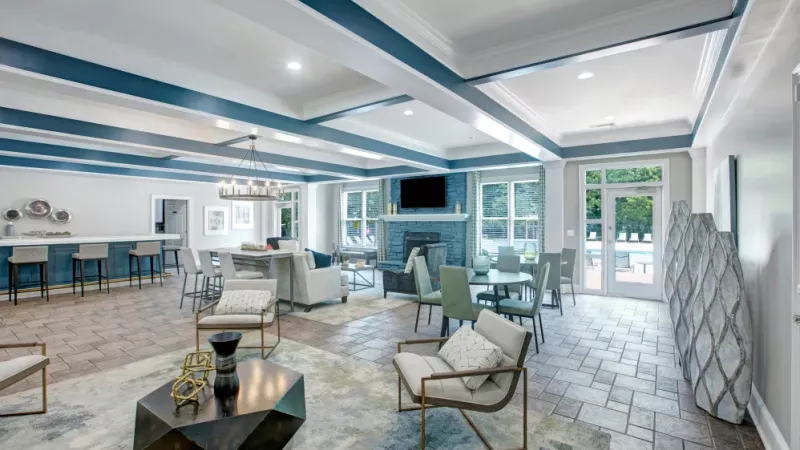 A spacious and modern clubhouse featuring comfortable seating, a fireplace, and large windows offering natural light and views of the outdoor amenities.