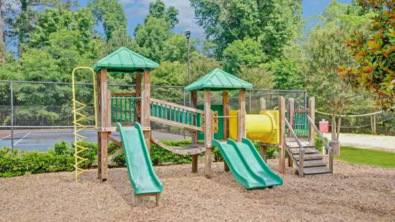 A colorful playground with slides and climbing structures, surrounded by lush greenery.