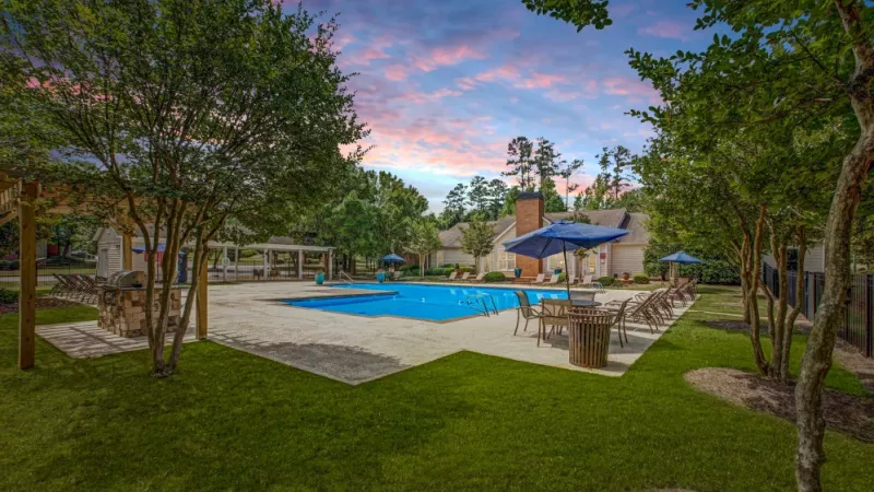 A wide view of the outdoor pool surrounded by lounge seating, lush greenery, and blue skies.