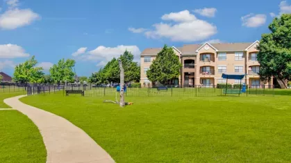 A walking path through a large open lawn area with pet amenities and residential units in the background.