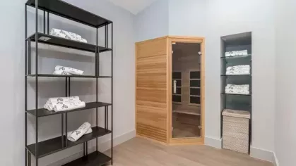 A sauna area with a neatly organized shelving unit holding towels and a wooden enclosed sauna cabin.
