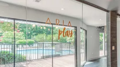 A recreational room with glass doors leading to the pool and the words "ARIA play" displayed on the glass.