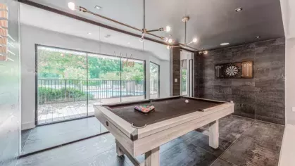 A billiards room featuring a sleek pool table, dartboard, and large windows overlooking an outdoor area.
