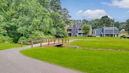 A picturesque walking path with a wooden bridge and green lawns leading to residential buildings.