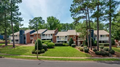 Apartment complex surrounded by tall pine trees and manicured grass.