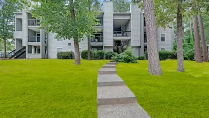 Tree-shaded pathway leading to a stylish multi-level apartment building.