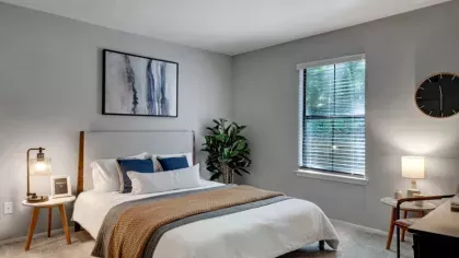 A serene bedroom with a neatly made bed, soft lighting, and a large window overlooking greenery.