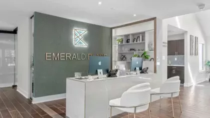 A stylish leasing office with sleek white furniture and "Emerald Place" branding on the wall.
