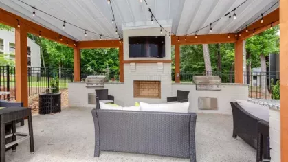 Outdoor covered seating area with string lights, a brick fireplace, and grills.