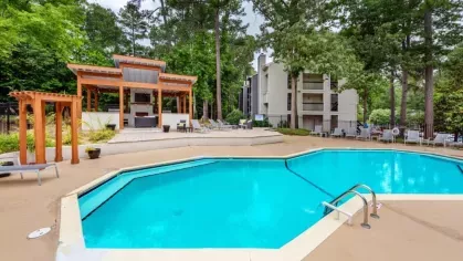 Bright turquoise swimming pool surrounded by trees and lounge chairs.