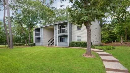 Open grassy area with a tree-lined path leading to a residential building.