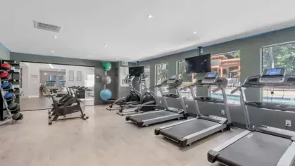 A modern gym with treadmills, exercise bikes, and bright windows overlooking a pool area.