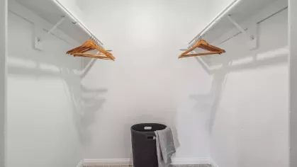 A spacious walk-in closet with ample hanging space, wooden hangers, and a laundry basket for storage.