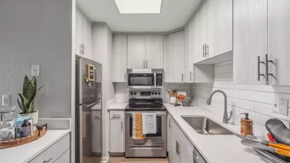 A sleek, modern kitchen featuring stainless steel appliances, white cabinetry, a subway tile backsplash, and bright natural lighting from a skylight.