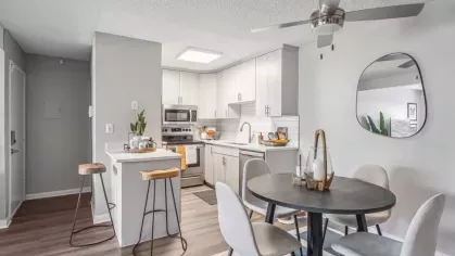 A stylish dining area adjacent to a sleek modern kitchen with white cabinetry, a subway tile backsplash, and natural lighting.