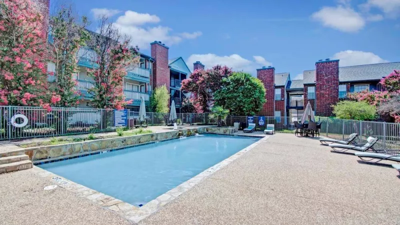 A large swimming pool with lounge chairs and vibrant greenery in the background.