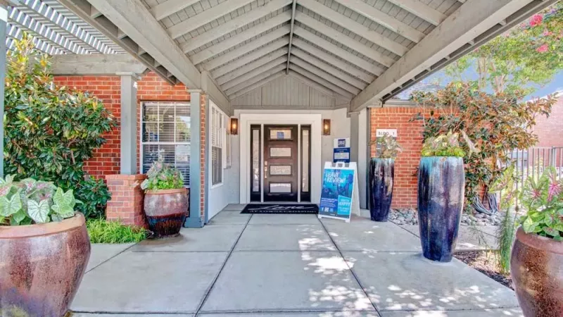 The entrance to a building with a welcoming covered walkway and large potted plants. 