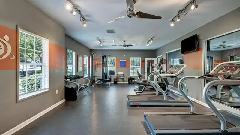 A spacious gym featuring various exercise equipment, including treadmills and machines, surrounded by walls and a ceiling. The floor is designed for fitness activities.