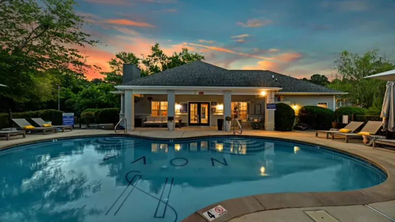 Outdoor pool with lounge chairs and clubhouse at sunset, showcasing amenities at Nova Chapel Hill apartments.