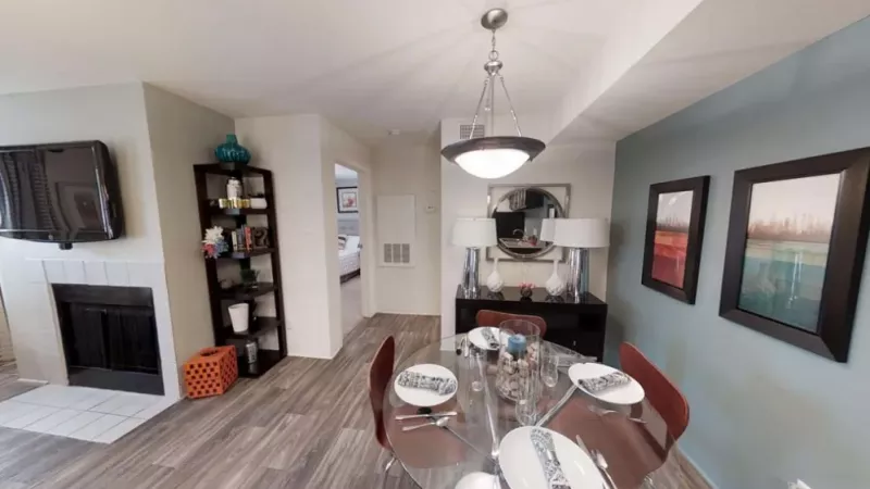 A dining room table set with plates and glasses, surrounded by chairs in a cozy indoor space with wooden flooring and ceiling fixtures.