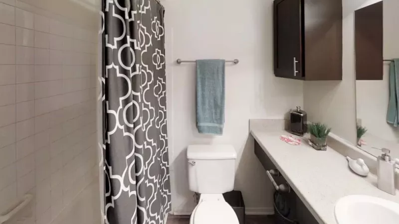 A bathroom featuring a shower curtain, with various fixtures such as a sink, toilet, and bathtub. The room has tiled walls and floor, along with a bathroom cabinet and mirror. The overall design is clean and modern.