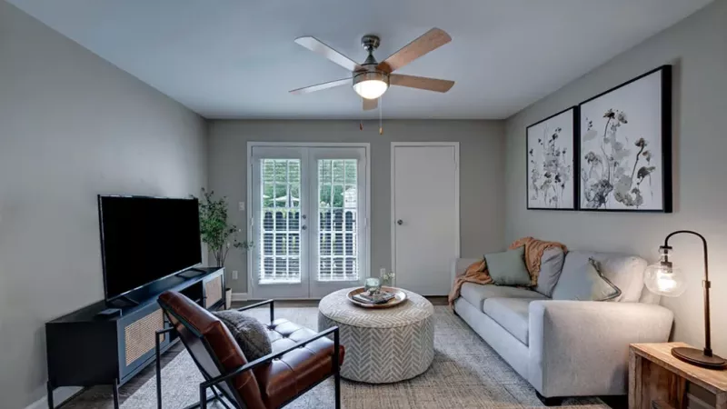 A cozy living room featuring a ceiling fan, a comfortable couch with decorative pillows, and various furnishings including a coffee table and cabinetry. The space has laminate wood flooring and is well-lit by natural light coming through the windows.