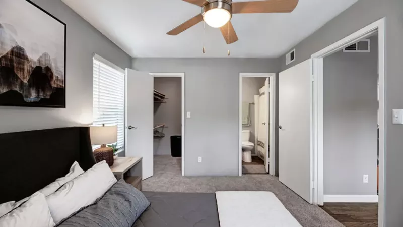 A cozy living room featuring a ceiling fan, with comfortable furniture including a sofa bed and pillows. The space has plaster walls and stylish flooring, creating a warm and inviting home atmosphere.