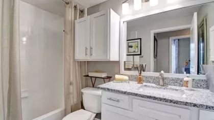 Spacious and inviting bathroom with granite countertops, white cabinetry, and modern lighting. The sleek design includes a shower/tub combination with elegant detailing and ample storage for a clean and functional space.