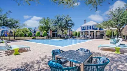 Expansive swimming pool area with comfortable lounge chairs, vibrant outdoor seating, and mature trees providing shade. A beautiful retreat for relaxation and recreation in a peaceful community setting.