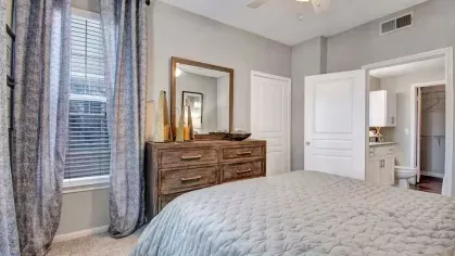 Elegant bedroom showcasing a large dresser, a mirror, and stylish decor. The space is filled with natural light from a window adorned with soft drapes, offering a perfect blend of functionality and comfort.