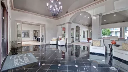 A luxurious clubhouse lobby with a chandelier, tiled floors, and elegant seating.
