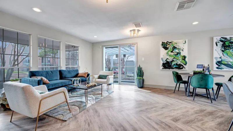  Spacious and modern community lounge featuring stylish seating, including a teal sofa and white armchairs, complemented by sleek decor and large windows that fill the space with natural light. The open layout and wood-style flooring create an inviting and vibrant atmosphere for gatherings or relaxation.