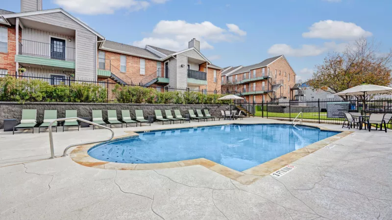  Outdoor pool area with comfortable lounge chairs and a clear blue sky. The pool is surrounded by a spacious patio and modern apartment buildings, creating a relaxing and inviting environment for residents.